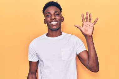 Genç Afro-Amerikalı günlük kıyafetler giymiş beş numarayı gösterip işaret ederken kendinden emin ve mutlu bir şekilde gülümsüyor.. 