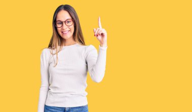 Güzel esmer, beyaz süveter giyen ve gözlüklü genç bir kadın başarılı bir fikri işaret ediyor. Heyecanlı ve mutlu. Bir numara.. 