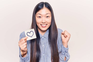 Genç, güzel Çinli kadın, elinde kalp şeklinde bir hatıra tutuyor gururla haykırıyor, zaferi kutluyor ve kollarını kaldırdığı için çok heyecanlı. 