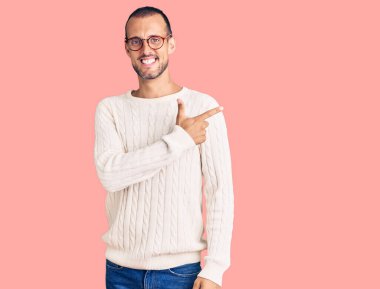 Gündelik kıyafetler ve gözlük takan genç yakışıklı bir adam. Yüzünde mutlu ve doğal bir ifadeyle, elleri ve parmaklarıyla yüzünü gösteren bir gülümseme var. 