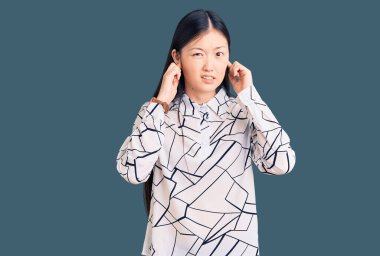 Gürültülü müzik sesi için kulaklarını parmaklarıyla kapatan sıradan bir tişört giyen genç, güzel Çinli kadın. sağır kavramı. 