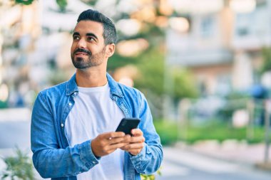 Genç İspanyol adam şehirde akıllı telefon kullanarak mutlu gülümsüyor..