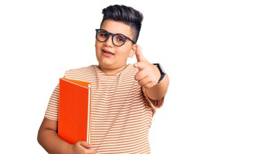 Küçük çocuk elinde gözlüklü, mutlu ve komik yüzüyle kamerayı işaret eden bir kitap tutuyor. iyi enerji ve titreşimler. 