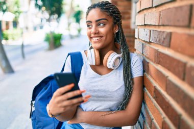 Genç Afrikalı Amerikalı öğrenci kampüste akıllı telefon kullanarak mutlu bir şekilde gülümsüyor.