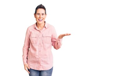 Kısa saçlı, günlük kıyafetler giyen neşeli bir şekilde gülümseyen ve avuç içi kameraya bakan genç bir kadın.. 