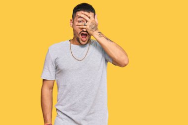 90 'lı yılların tarzında dövmeleri olan yakışıklı bir adam. Şoka girmiş, yüzünü ve gözlerini kapamış, utangaç ifadesiyle parmaklarının arasından bakıyor.. 