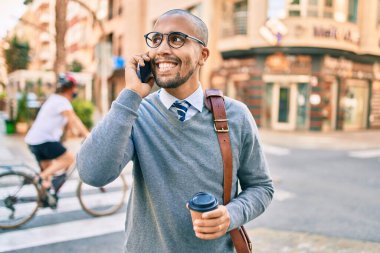 Genç Afrikalı Amerikalı iş adamı akıllı telefondan konuşuyor ve şehirde kahve içiyor..