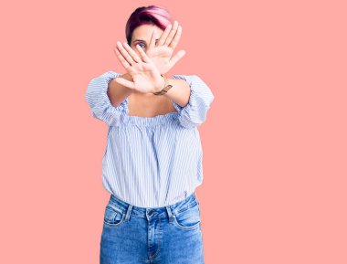 Pembe saçlı genç bir kadın. Günlük kıyafetler giyiyor. Reddedilmiş yüz ifadesi. 