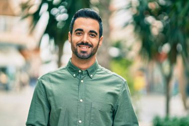 Genç İspanyol adam gülümseyerek şehirde mutlu mesut dikiliyor..