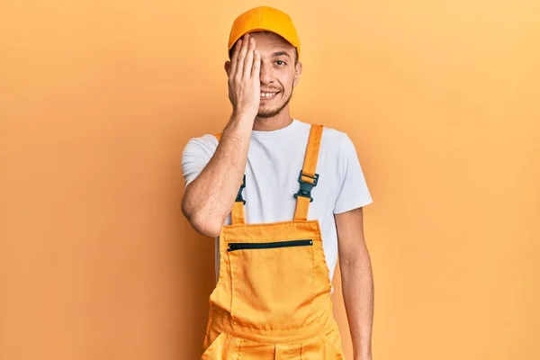 ヒスパニック系の若い男は手で一つの目をカバーする手織りの制服を着て 顔に自信を持って笑顔と驚きの感情 — ストック写真