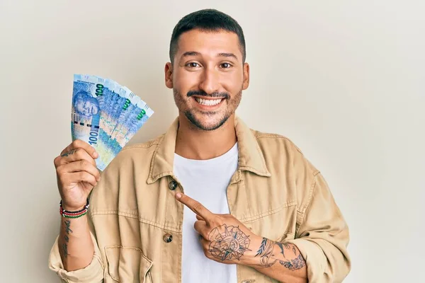一个英俊的男人 身上有纹身 手里拿着100兰特的南非钞票 高兴地微笑着 手指手画脚 — 图库照片