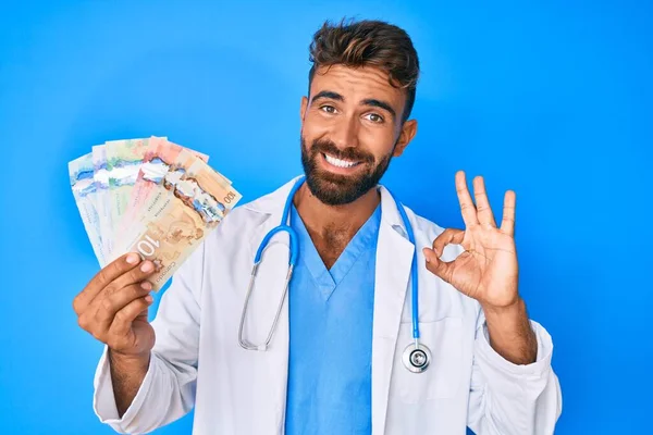 Молодий Гізпанічний Чоловік Формі Лікаря Тримаючи Канадійські Долари Плакаті Посміхається — стокове фото