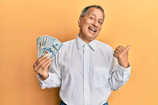 Hombre Indio Mediana Edad Sosteniendo Dólares Apuntando Pulgar Hacia Lado —  Fotos de Stock