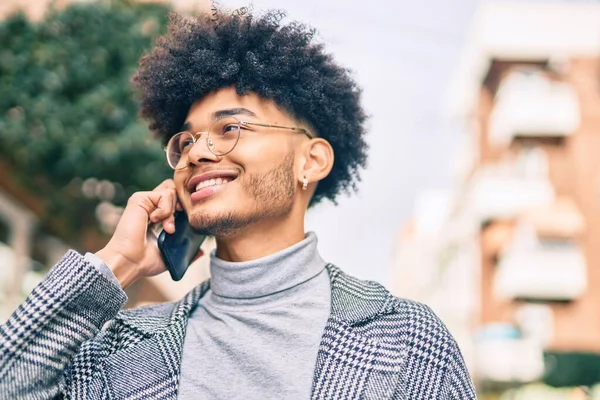 Genç Afrikalı Amerikalı iş adamı gülümsüyor. Şehirdeki akıllı telefondan mutlu bir şekilde konuşuyor..
