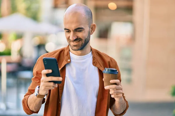 Young hispanic bald man using smartphone drinking coffee at the city.