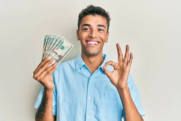 Joven Hombre Afroamericano Guapo Sosteniendo Billetes Dólares Haciendo Señal Bien —  Fotos de Stock