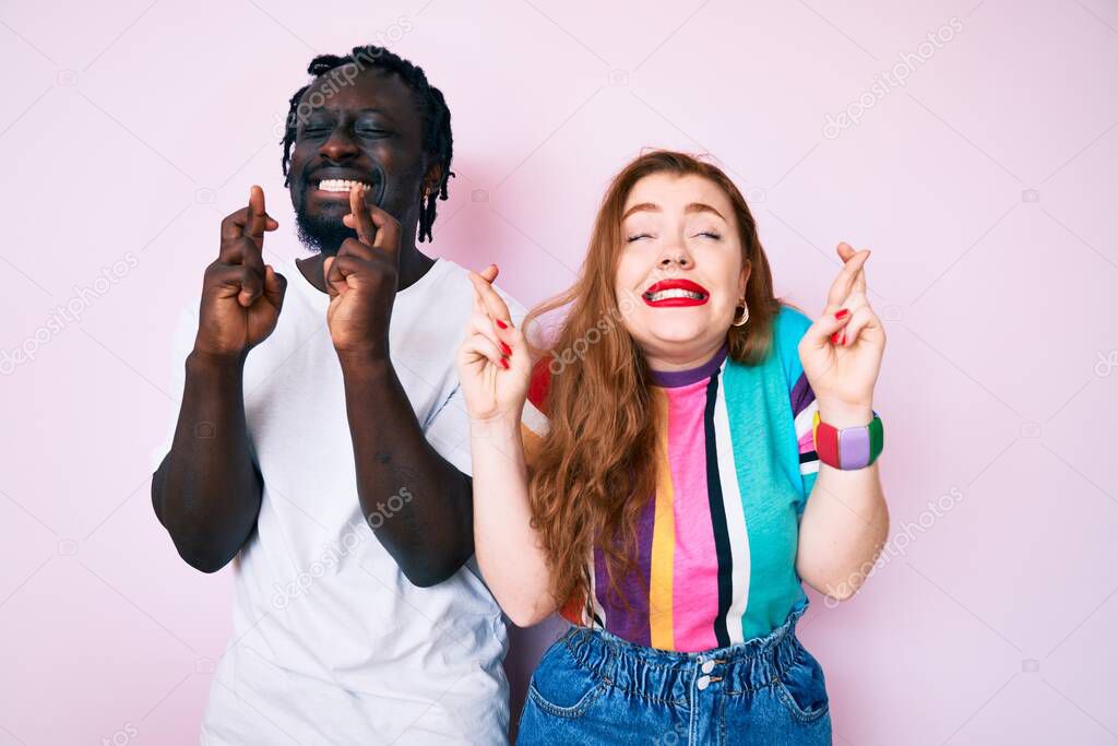 Interracial couple wearing casual clothes gesturing finger crossed smiling with hope and eyes closed. luck and superstitious concept. 