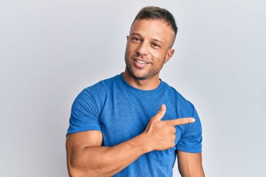 Yakışıklı, sıradan kıyafetler giyen, neşeli gülümseyen, elleri ve parmakları yanda olan kaslı adam. 