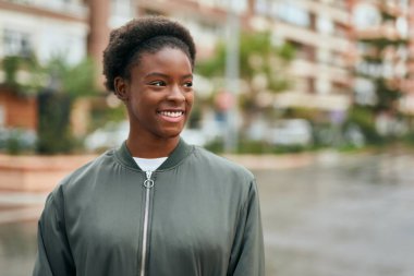 Genç Afrikalı Amerikalı kız gülümseyerek şehirde mutlu mesut duruyor..