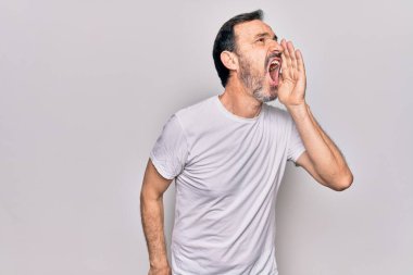 Orta yaşlı yakışıklı bir adam, günlük tişört giyip izole edilmiş beyaz arka planda durmuş el ele tutuşarak bağırıyor ve bağırıyordu. İletişim konsepti.