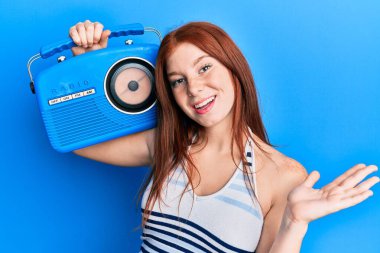 Genç kızıl saçlı kız klasik bir radyo ile başarıyı kutluyor mutlu bir gülümsemeyle ve kazanan bir ifadeyle elini kaldırarak. 