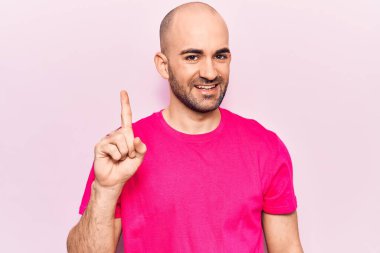 Genç, yakışıklı, kel bir adam, günlük tişört giyip gülümsüyor, bir fikir ya da soruyla gülümsüyor ve mutlu bir yüzle işaret ediyor. 