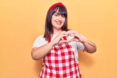 Önlük takan genç ve cüsseli bir kadın. Sevgiyle gülümsüyor. Elleriyle kalp sembolü ve şekli gösteriyor. romantik kavram. 