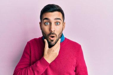 Gündelik kıyafetler giyen genç İspanyol adam, elleri çenesinde, inanamama, şaşkınlık ve şaşkınlık dolu bir ifade takınıyor. 