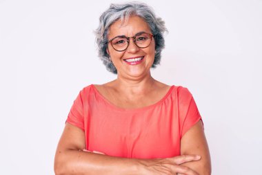 Son sınıf İspanyol asıllı, gri saçlı, sıradan kıyafetler giyen ve gözlüklü mutlu yüzlü, kollarını kavuşturup kameraya bakan bir kadın. pozitif kişi. 