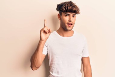 Bir fikir veya soruyla gülümseyen gündelik kıyafetler giyen genç İspanyol adam, bir numara, mutlu bir yüzle işaret ediyor. 
