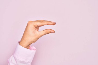 İzole edilmiş pembe arka plan üzerinde parmaklarını gösteren beyaz bir adamın eli. Görünmez bir şeyi alıp, parmaklarıyla uzayı gösteren bir nesneyi tutuyor.