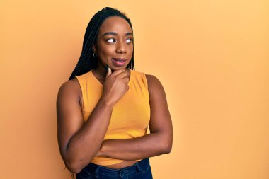 Elleri çenesinde gündelik giysiler giyen genç Afrikalı Amerikalı kadın soru sormayı düşünüyor, düşünceli bir ifade. Düşünceli bir yüzle gülümsüyor. şüphe kavramı. 