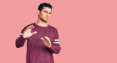 İspanyol asıllı yakışıklı genç adam, günlük giysiler giymiş, tiksindirici bir ifade takınıyor, tiksindirici bir yüz ifadesi takınıyor ve tiksindirici bir ifade takınıyor. Eller havada. 