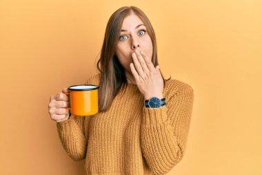 Güzel, beyaz bir kadın bir fincan kahve içiyor. Ağzını eliyle kapatıyor. Şok geçiriyor ve hata yapmaktan korkuyor. şaşırmış ifade 