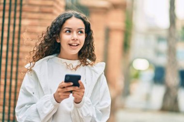Güzel İspanyol kız şehirde akıllı telefon kullanarak mutlu gülümsüyor..