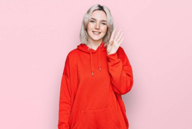 Genç sarışın kız gündelik giysiler giyer ve parmaklarıyla dört numarayı gösterir ve gülümserken kendinden emin ve mutludur.. 