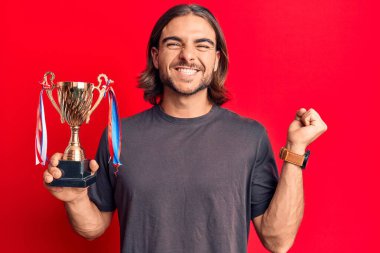 Genç yakışıklı adam kupayı tutuyor. Gururla bağırıyor, zaferi kutluyor ve başarıyı kollarını kaldırarak kutluyor. 