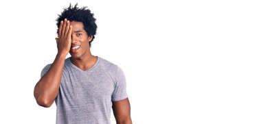 Yakışıklı Afro saçlı, sıradan kıyafetler giyen, bir gözünü eliyle kapatan, yüzünde kendine güvenen gülümseme ve sürpriz duygular taşıyan Afro-Amerikan bir adam.. 