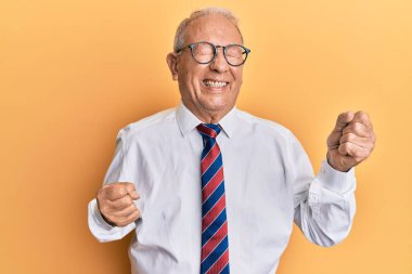 İş kıyafetleri giyen kıdemli beyaz adam kolları havada ve gözleri kapalı bir şekilde başarıyı kutluyor ve şaşırıyor. 