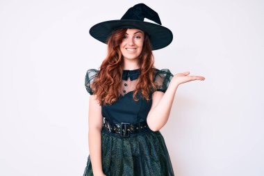 Cadı cadılar bayramı kostümü giymiş genç ve güzel bir kadın. Neşeli bir şekilde gülümsüyor ve avuç içi kameraya bakıyor.. 