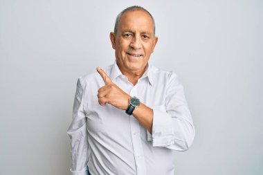 Yakışıklı, beyaz tişörtlü, neşeli, yüzünde gülümseme olan, mutlu ve doğal bir ifadeyle elini ve parmağını yana doğru gösteren bir adam. 