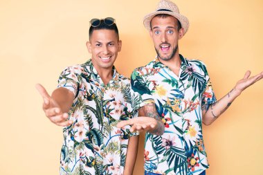 Yaz şapkası ve Hawaii tişörtü giyen iki genç eşcinsel. Kolları açık gülümsüyor. Dostça karşılama, olumlu ve kendinden emin selamlar. 