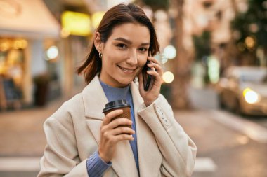 Genç İspanyol kadın gülümsüyor. Şehirdeki akıllı telefondan konuşuyor..