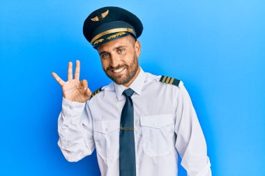 Uçak pilotu üniforması giyen sakallı yakışıklı adam gülümsüyor ve el ve parmaklarıyla 