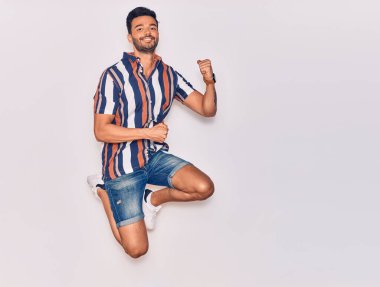 Genç, yakışıklı, sıradan kıyafetler giyen, mutlu gülümseyen bir İspanyol. Yüzünde tebessümle zıplıyor, beyaz arka planda yumruklar havada kutluyor.