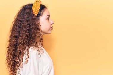 Kıvırcık saçlı, sıradan kıyafetler giyen, rahat bir görünüm takınan, kendine güveni olan güzel bir kız çocuğu.. 