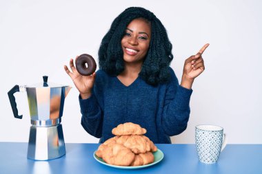 Güzel Afrikalı kadın kahvaltısını yapıyor çikolatalı donutla gülümsüyor mutlu bir şekilde elini ve parmağını yana uzatıyordu. 