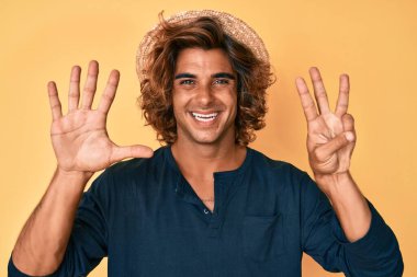 İspanyol asıllı genç adam, yaz şapkası takıyor ve 8 numaralı parmaklarını göstererek gülümsüyor. Kendinden emin ve mutlu.. 