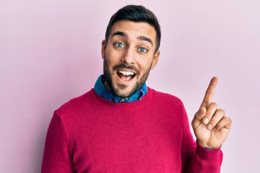 Yüzünde kocaman bir gülümseme olan, gündelik kıyafetler giyen genç İspanyol adam, kameraya el ile işaret ediyor.. 