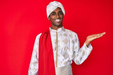 Gelenek giyinmiş yakışıklı Hintli adam Sherwani sari giysileri içinde neşeli bir şekilde sunum yapıyor ve avuç içi kameraya bakıyor.. 